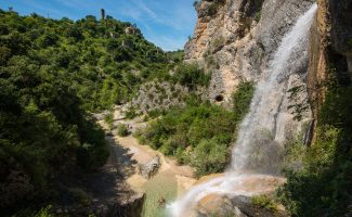 See the famous Rochecolombe waterfall flowing down the river